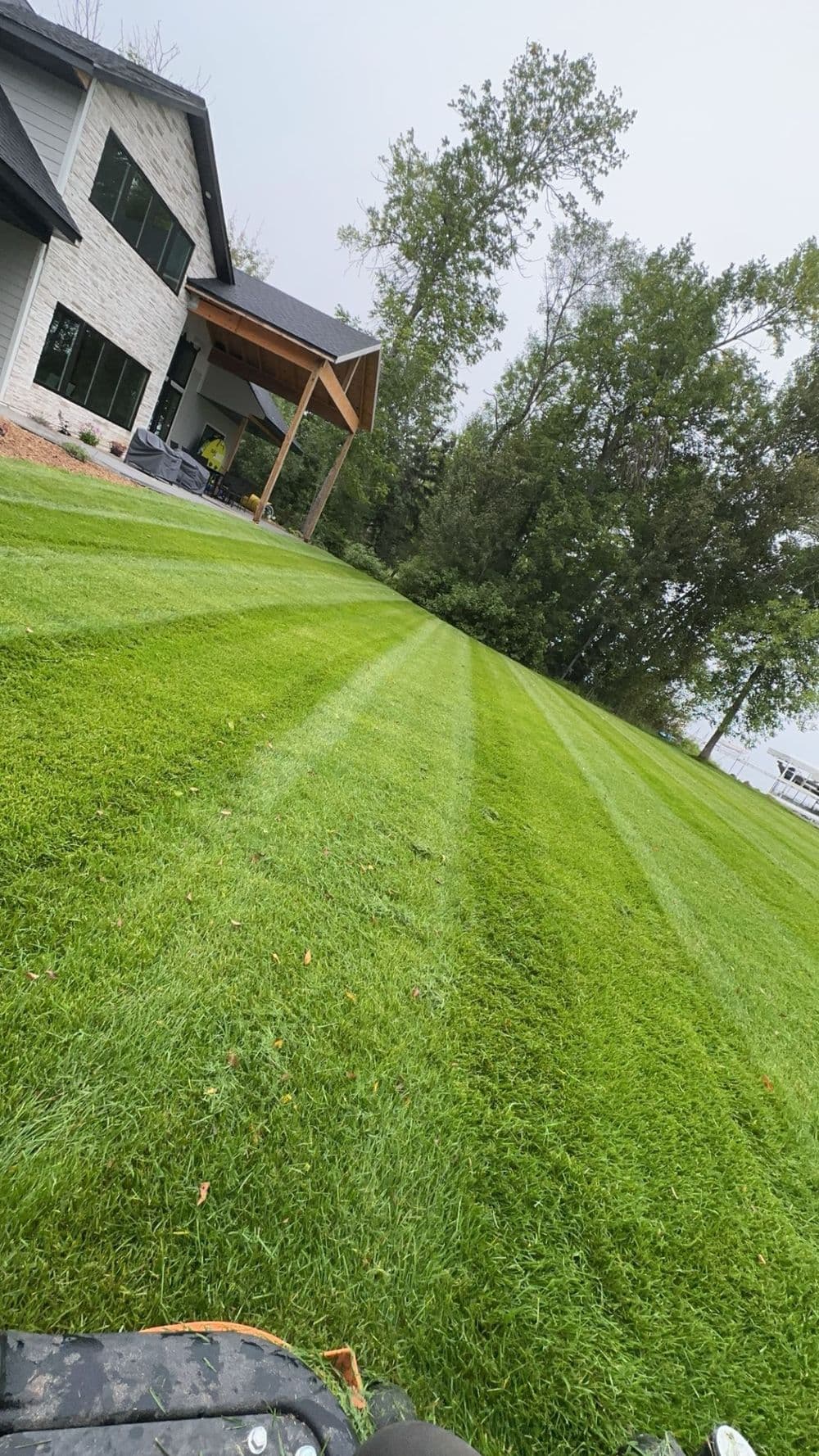 Freshly mowed lawn with striped patterns beside a modern home and trees.