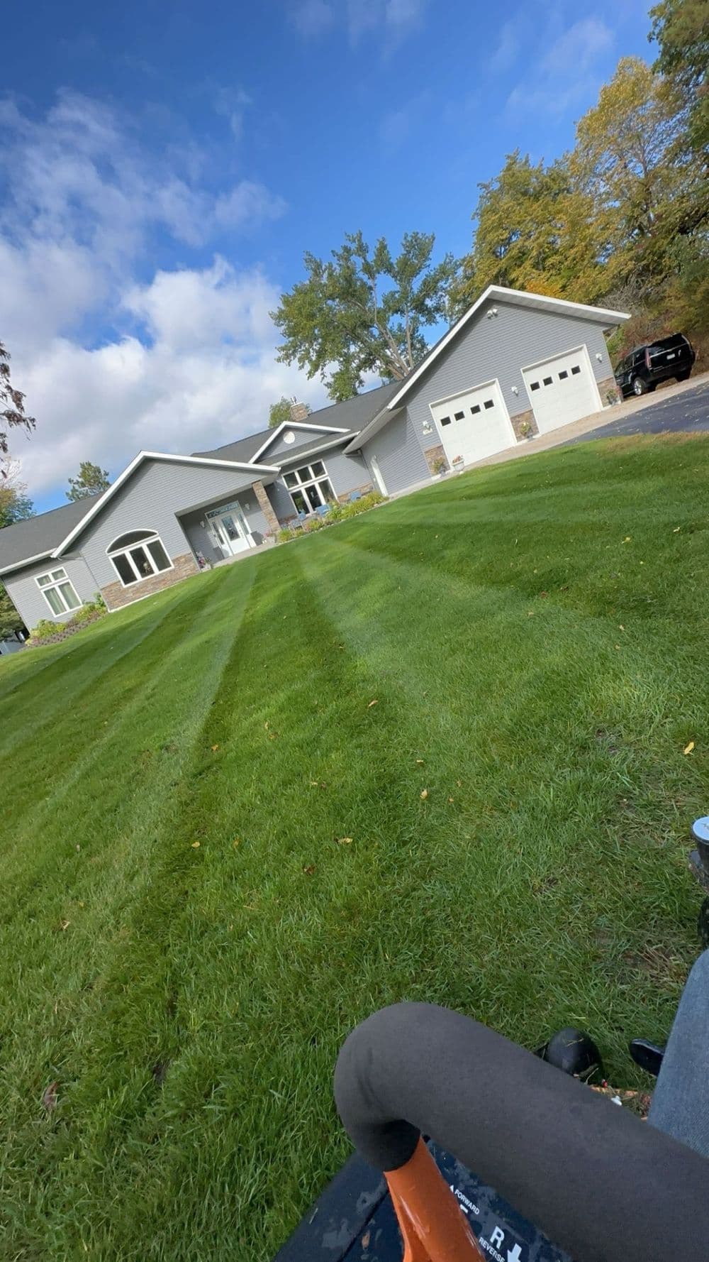 Modern gray house with manicured lawn and blue sky, showcasing curb appeal and landscaping.
