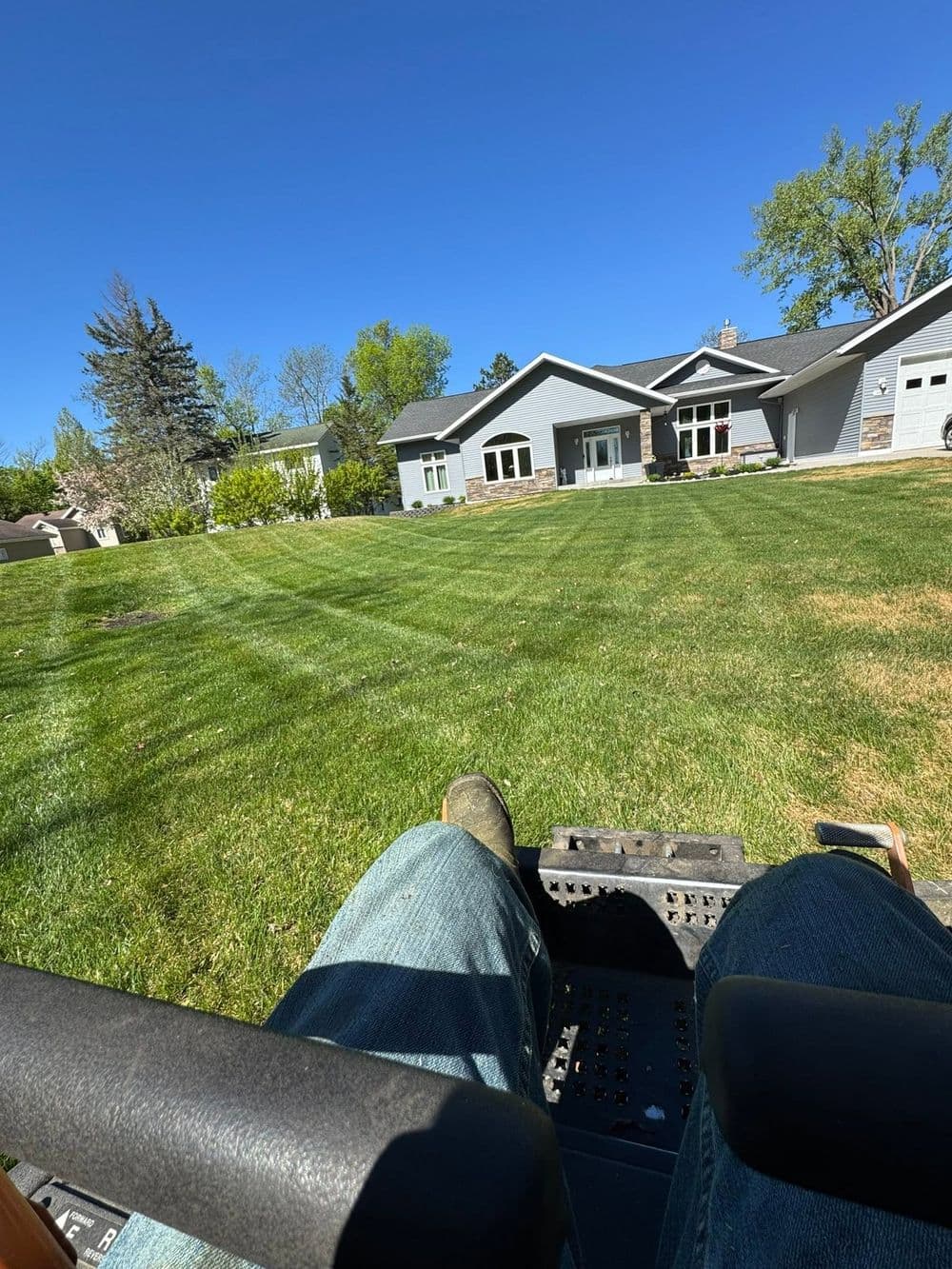 Person on a lawn mower cutting a green lawn in front of a modern house on a sunny day.