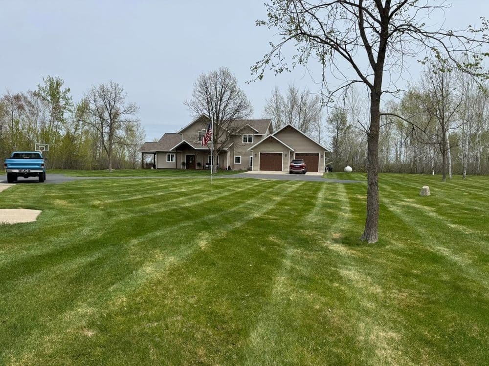 Well-maintained home with a manicured lawn and driveway, surrounded by trees.