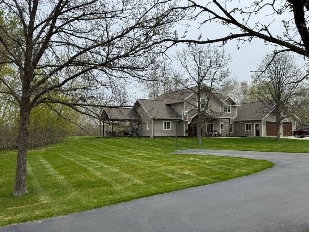 Modern family home with well-maintained lawn and trees, featuring a driveway and basketball hoop.