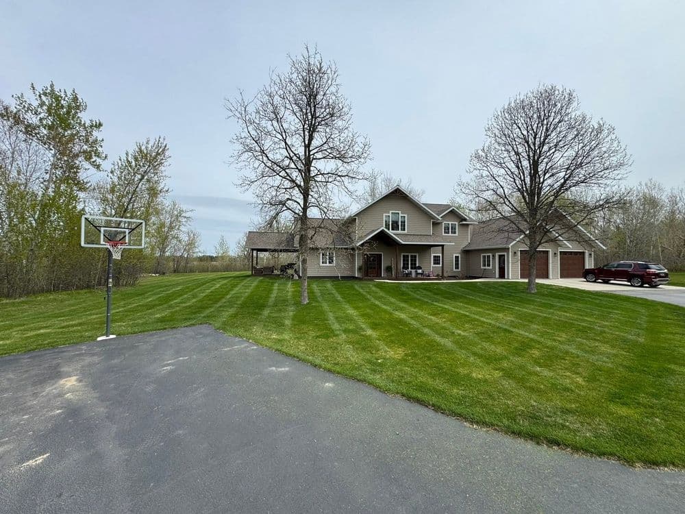 Suburban home with a manicured lawn and basketball hoop, surrounded by trees.