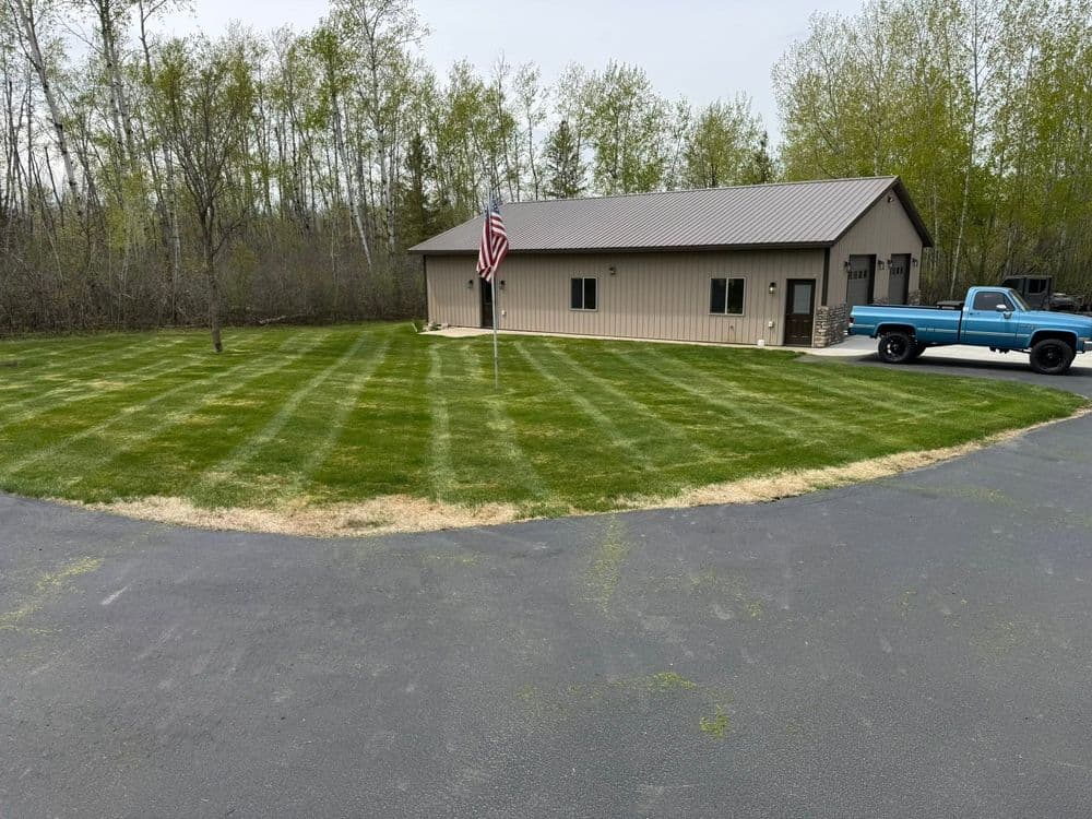 Neatly manicured lawn with a blue truck and a modern building in a wooded area.