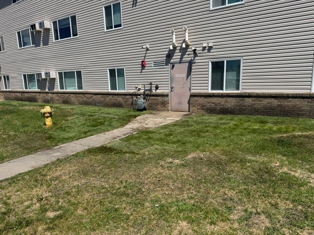 Apartment building exterior with green lawn, sidewalk, and yellow fire hydrant.