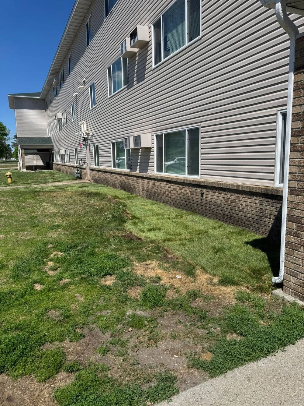 Residential building with grassy area and air conditioning units on the exterior wall.